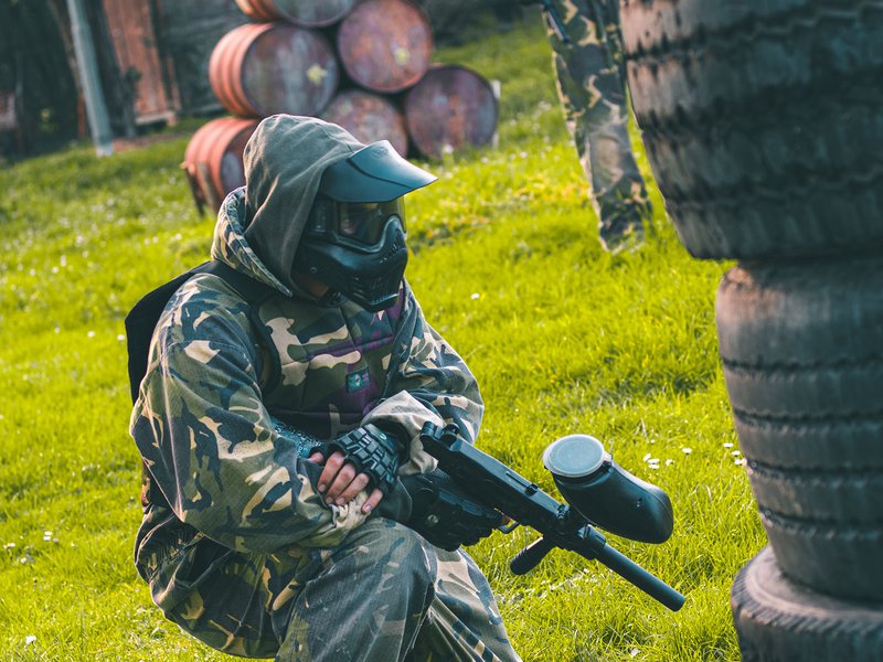 Giocatore di paintball accovacciato dietro un riparo, marcatore in mano